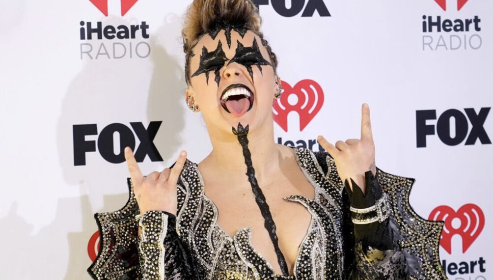 JoJo Siwa with kiss makeup on and her two hands doing the rock and roll sign. 